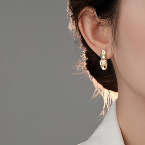 Close-up of a model wearing an asymmetrical irregular gold lava earring with a metallic finish