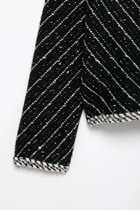 Detail of black knitted jacket with white stripes and braided trim on cuffs and hem