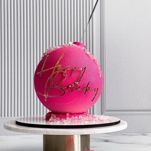 Macro shot of pink spherical cake topper with golden Happy Birthday lettering and glitter