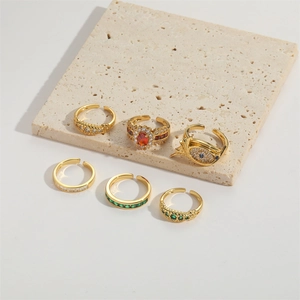 Set of six gold open rings with colorful zircon stones on a beige textured stone block