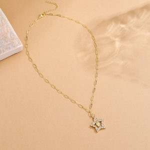 Gold star pendant necklace with cubic zirconia and paperclip chain on stone surface