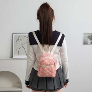 Detail of pink plaid quilted mini backpack featuring blue bow embroidery and straps