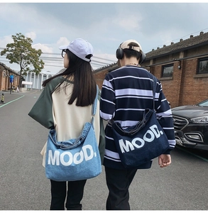 Detail of light and dark blue denim messenger bags with MOOD print on street models