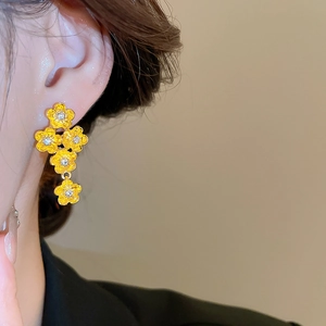 Detailed close-up of golden flower drop earrings with sparkling white zircons worn on model