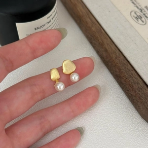 Detail of matte gold brushed metal earring with round pearl held by model fingertips