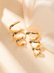 Detailed view of gold spiral earrings on beige surface with champagne silk background
