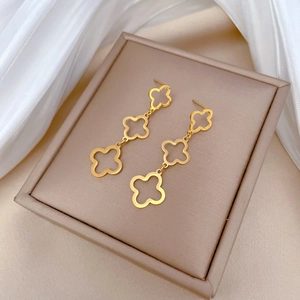 Detailed macro of gold clover tassel earrings on a champagne leather jewelry box