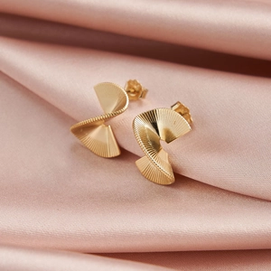 Close-up of golden irregular spiral leaf earrings on pink silk background