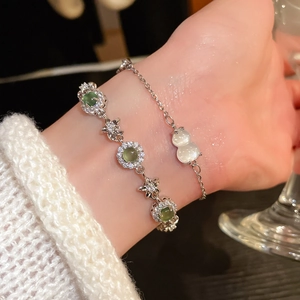 Detail of layered silver bracelets with green gemstones and white gourd charm on wrist