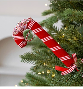 Macro detail of red and white striped candy cane ornament with sequins and a bow on tree
