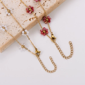 Golden daisy floral necklaces with red and white beads draped over stone on white background