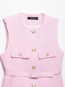 Détail d'un gilet en tweed rose avec boutons dorés et ceinture assortie sur blanc