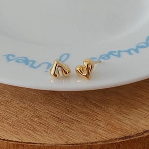 Detailed view of polished gold heart-shaped stud earrings on a white ceramic tray