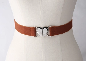 Détail d'une ceinture élastique marron avec une boucle métallique argentée en forme de cœur