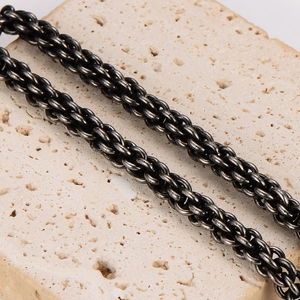 Retro stainless steel woven twist chain necklace for men on a textured beige stone background