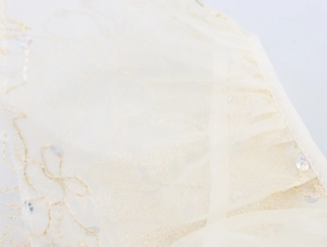 Détail macro du tulle champagne avec broderies dorées et paillettes brillantes