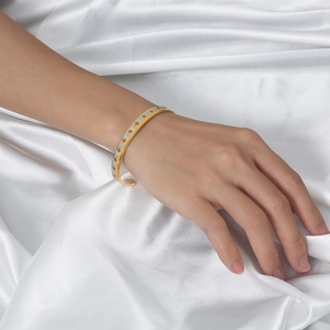 Detail view of gold open cuff bangle with colorful geometric enamel on white silk