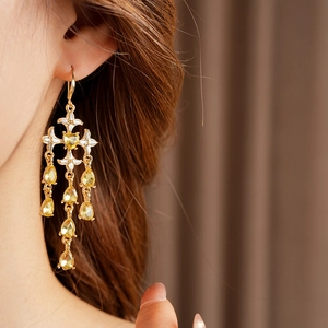 Macro detail of gold-plated cross earrings with yellow pear-cut crystals and diamonds