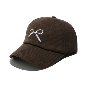 Detail of dark brown corduroy baseball cap with white bow embroidery and textured fabric