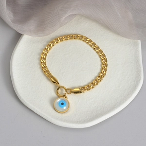 Golden Cuban chain bracelet with Evil Eye pendant on a minimalist white textured plate
