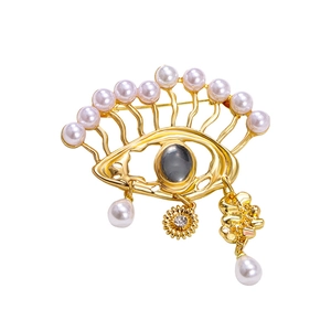 Artistic eye-shaped brooch with golden metal frame, pearls, and teardrop charms