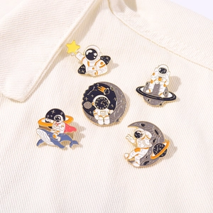 Close-up of five enamel astronaut pins on off-white corduroy fabric texture