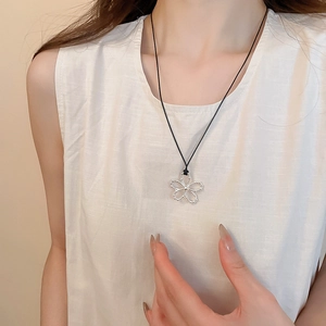 Détail du pendentif fleur argentée évidée sur cordon noir porté par un mannequin