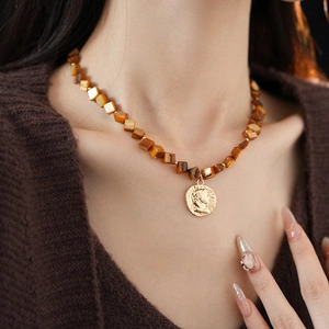 Close-up of vintage golden portrait coin necklace with amber resin beads on model