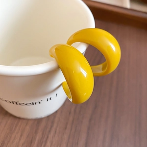 Gros plan de boucles d'oreilles créoles jaunes en résine sur le bord d'une tasse