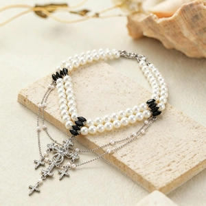Detail of layered pearl necklace with ornate rhinestone cross pendants on stone base