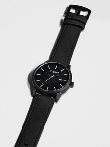 Close-up of minimalist black watch with leather strap, date window and matte finish
