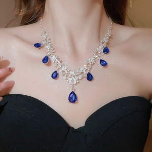 Model wearing a silver necklace with sparkling teardrop blue gemstones in royal style