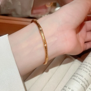 Close-up of a gold wavy cuff bracelet with embedded zircons worn on a wrist