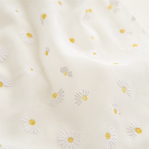 Macro detail of creamy white chiffon fabric with exquisite 3D embroidered daisy floral patterns