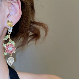 Dettaglio di orecchini a fiore con cristalli rosa e perle indossati da una modella