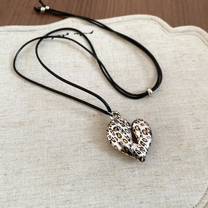 Detail of a leopard print heart pendant on a wax cord necklace with silver bead accents