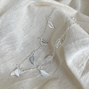 Close-up of 925 sterling silver anklet featuring leaf charms on linen fabric