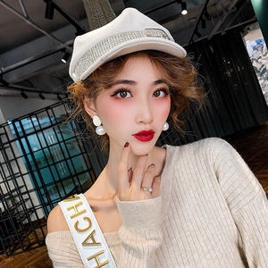 Close-up of elegant pearl earrings worn with a white rhinestone baker boy cap and sweater