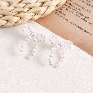 Detail view of handmade pearl bow earrings with intricate woven floral texture on white background
