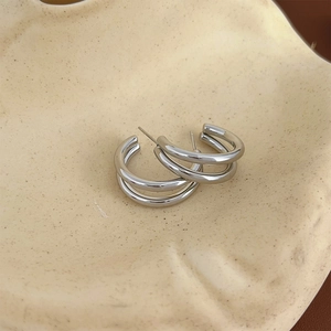 Macro shot of triple-layer C-shaped silver earrings on an aesthetic ceramic plate