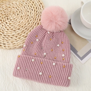 Pink knitted beanie hat for women featuring pearls and a large soft faux fur pompom decor