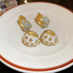 Detail of C-shaped enamel flower earrings in blue and white on a ceramic plate