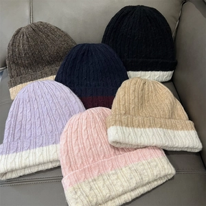 Stack of chunky knit beanies in multiple contrast colors including purple and beige