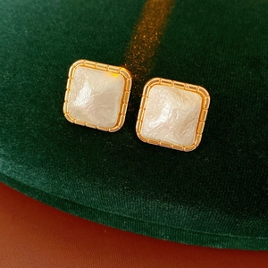 Detail view of square gold earrings with white pearlescent inlay on green velvet