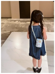 Girl wearing a blue cylinder bucket bag with red cherry print and gold chain strap