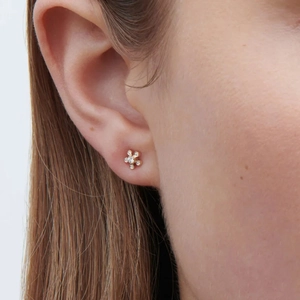Detailed close-up of a model wearing a gold floral stud earring with clear zircon stones