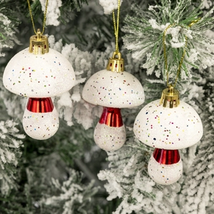 Glittery white mushroom Christmas tree ornaments with red accents hanging on a snowy branch