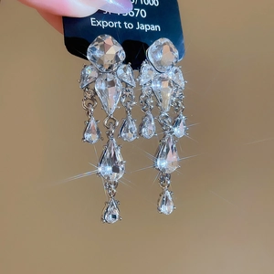 Dettaglio macro di orecchini geometrici a nappa d'argento con cristalli lucenti