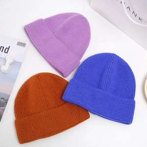 Detailed knit texture of solid purple, blue, and caramel winter beanies for unisex