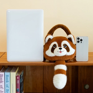 Plush raccoon handbag shown next to a laptop and phone to illustrate the compact size